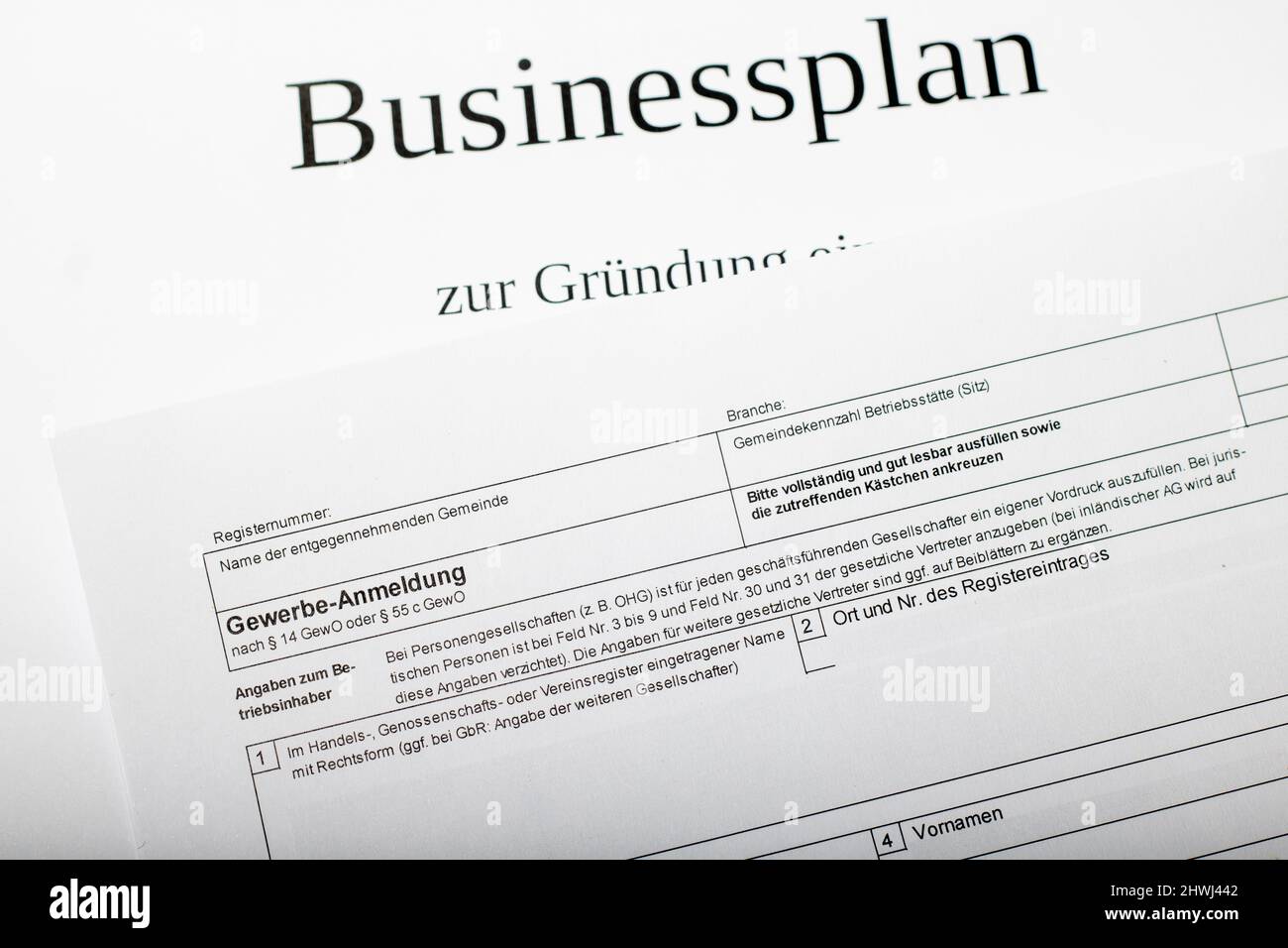 Das deutsche Standardformular für die Geschäftsanmeldung in deutscher Sprache bei der Stadt oder Gemeinde liegt auf einem Businessplan für den Start der Selbständigung Stockfoto