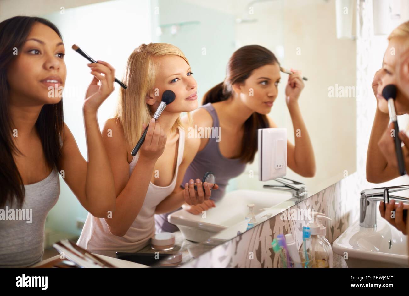 Beauty Queens. Aufnahme von drei Freunden, die sich vor dem Spiegel schminken. Stockfoto