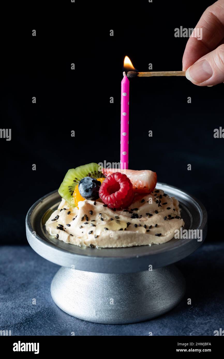 Eine Hand zündet eine Kerze auf einem hausgemachten Baiser mit Fruchtauflagen an. Stockfoto