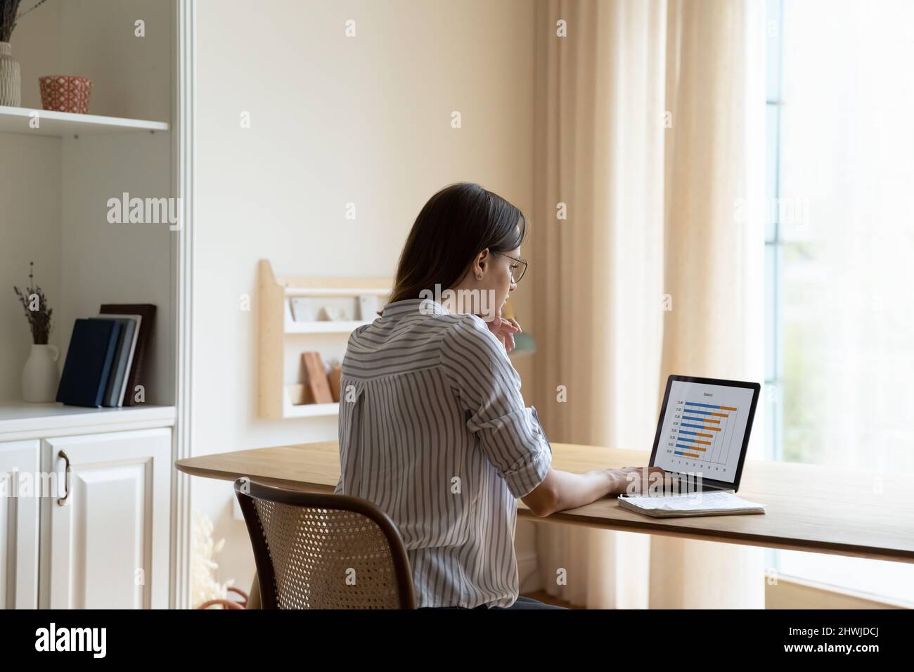 Rückständig lernt eine nachdenkliche Geschäftsfrau Diagramme, Verkaufsstatistiken auf einem Laptop Stockfoto
