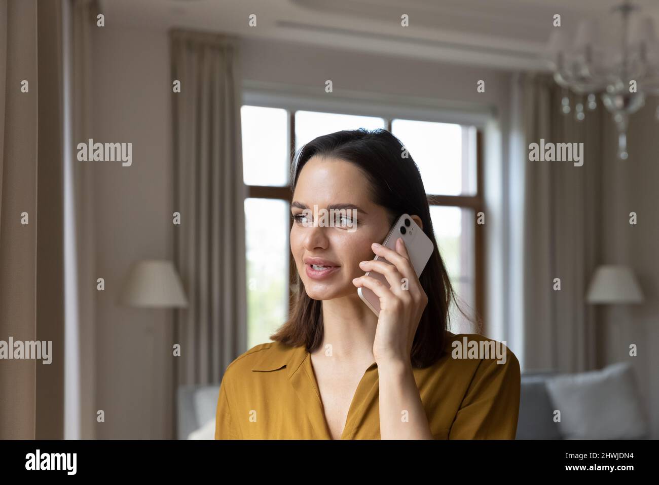 Junge Frau, die im luxuriösen Wohnzimmer steht, spricht auf dem Smartphone Stockfoto