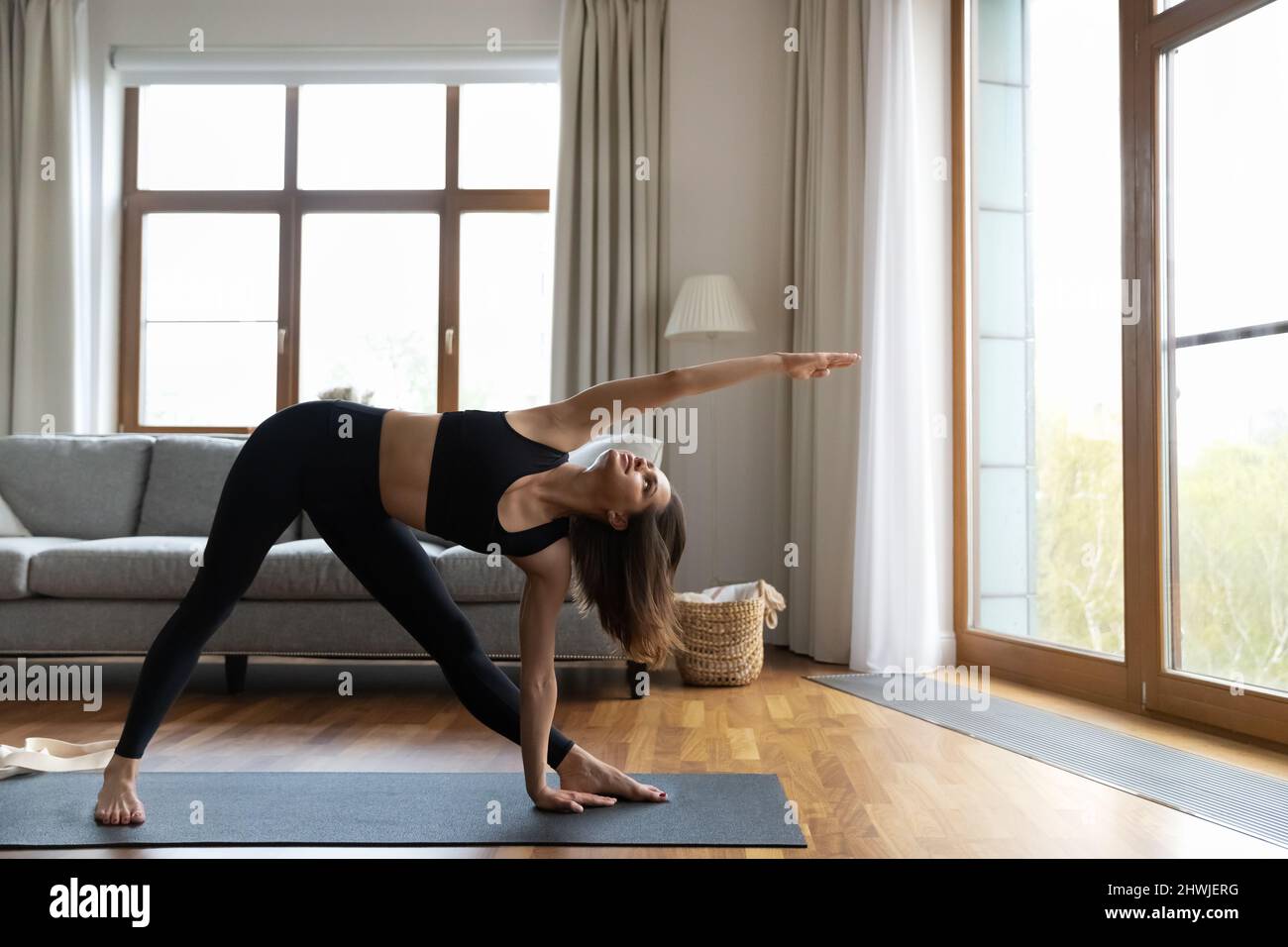 Junge Frau in modischer, bequemer Sportkleidung, die zu Hause Yoga praktiziert Stockfoto