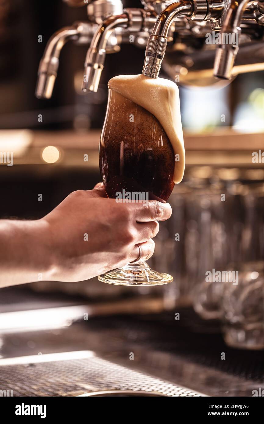 Schaum gießt das Glas eines frisch gezapften dunklen Bieres in einem Pub oder Restaurant herunter. Stockfoto