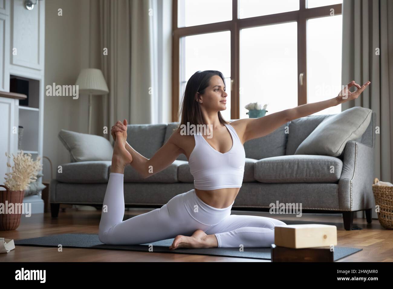 Junge Frau in weißer Sportkleidung, die zu Hause Yoga-Asanas praktiziert Stockfoto