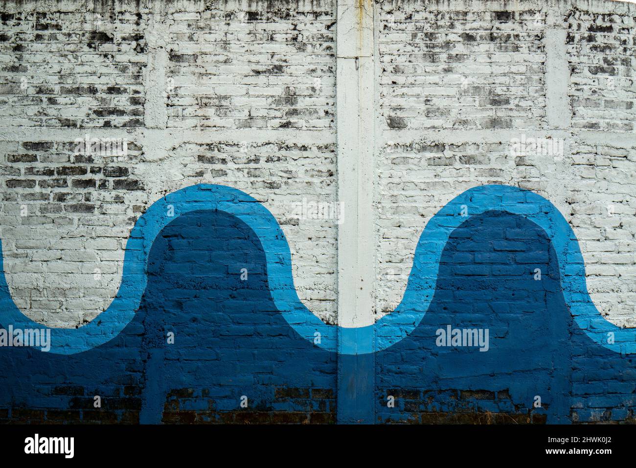 Graffiti auf einer Ziegelwand mit blauem Wellenmuster. Verwitterter alter weißer Backsteinwand Stockfoto