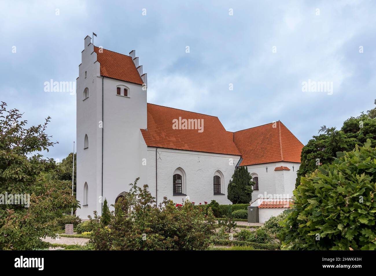 Weiße skandinavische Kirche mit einem hohen Turm und einem orangefarbenen Ziegeldach gegen den blauen Himmel, Orslev, Dänemark, 9. August 2021 Stockfoto