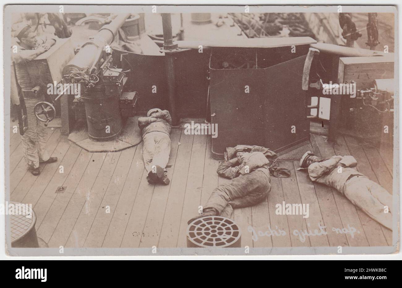 „Jack's Quiet Nap“: Fotopostkarte mit drei Matrosen der Royal Navy, die auf Deck des Schlachtschiffs HMS Jupiter liegen. Ein vierter Seemann steht neben einem Decksgewehr. Das Bild stammt aus dem frühen 20.. Jahrhundert (Ära des Ersten Weltkriegs) Stockfoto