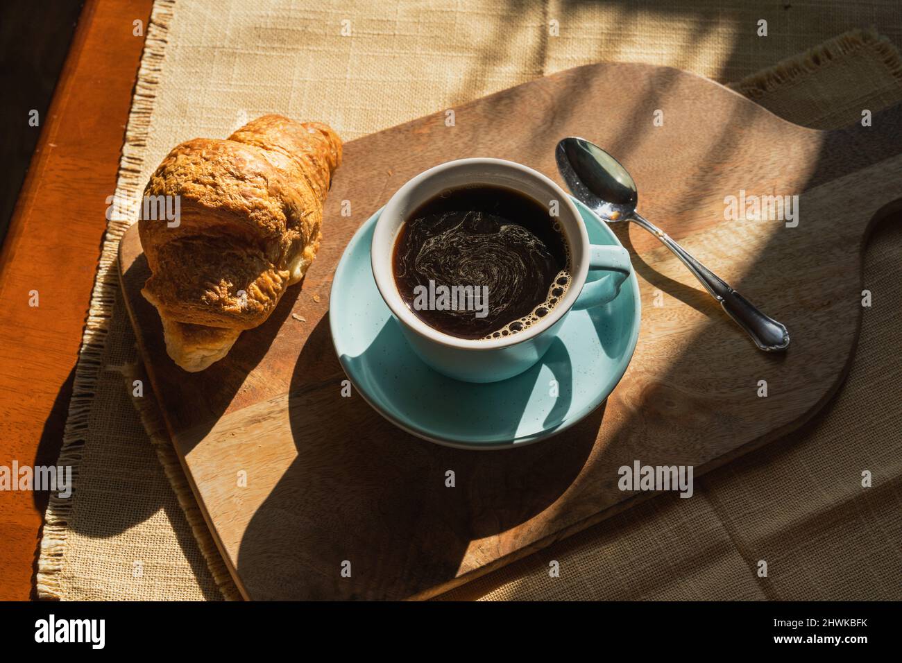 Tasse Kaffee, Croissant, vom Sonnenlicht beleuchtet, flach liegend, Blick von oben. Stockfoto