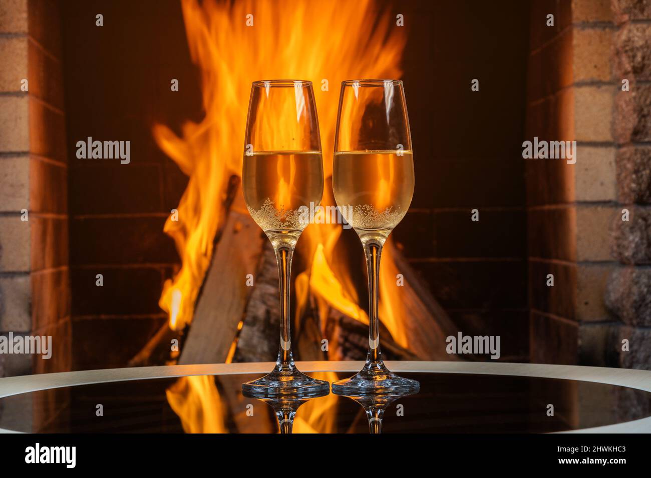 Zwei Gläser Champagner neben einem gemütlichen Kamin in einem Landhaus mit Spiegelung an einer Glasoberfläche. Stockfoto