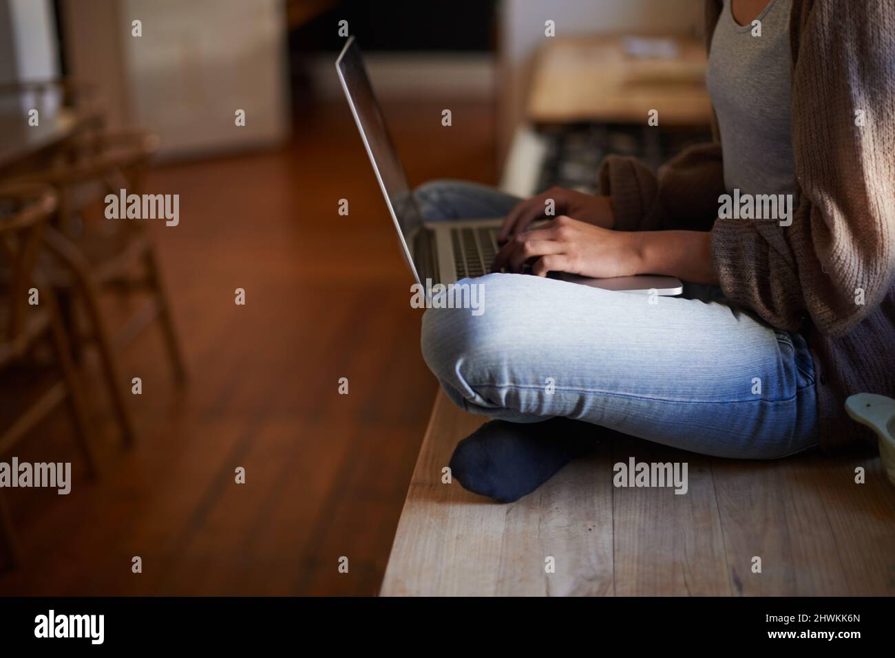 E-Mails am Morgen. Zugeschnittenes Bild einer Frau, die auf einem Tresen sitzt und auf ihrem Laptop tippt. Stockfoto