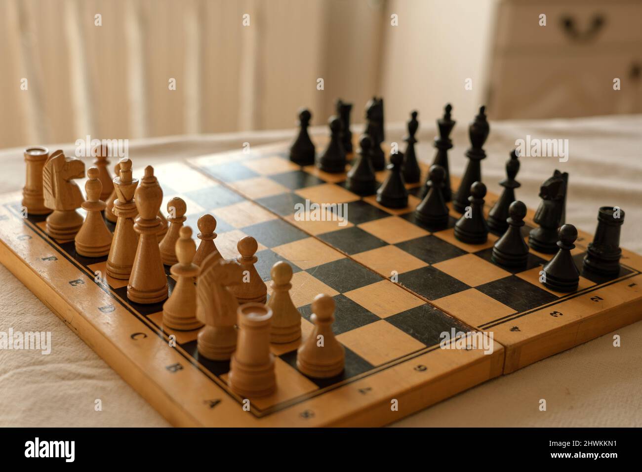 Hölzerne Schachfiguren stehen in einer Reihe auf einem alten Schachbrett Anfang des Spiels. Stockfoto