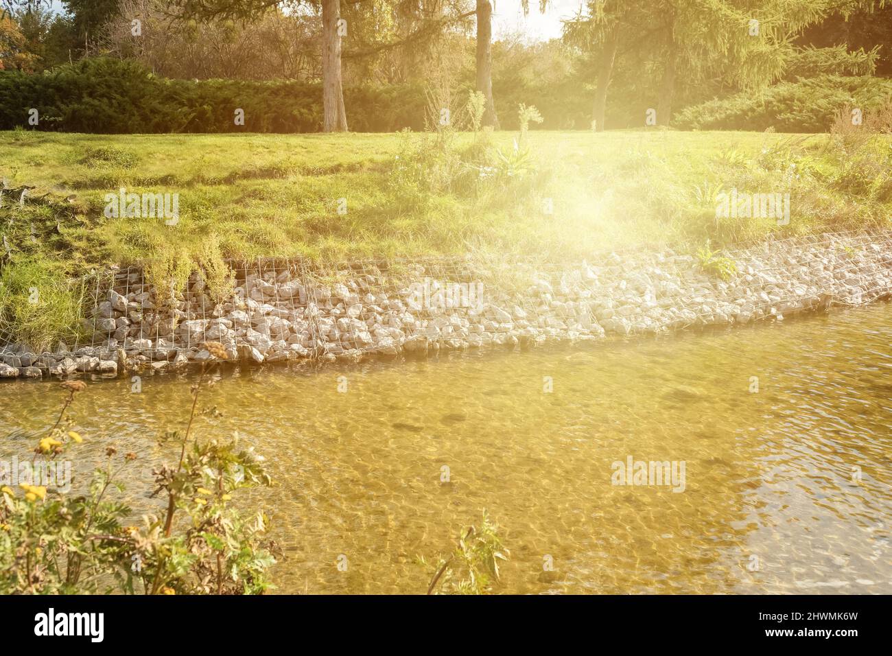 Stärkung der Ufer des Flusses, Mesh und Steine. Landschaft Flussufer und große Steine mit Metallgeflecht. Sonnenblendung Stockfoto