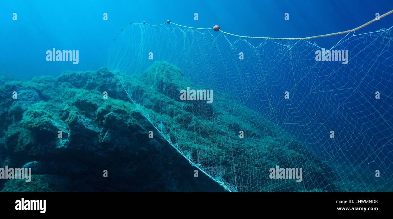 Fischernetz unter Wasser Gillnet im Meer mit Felsen und blauem Wasser Stockfoto