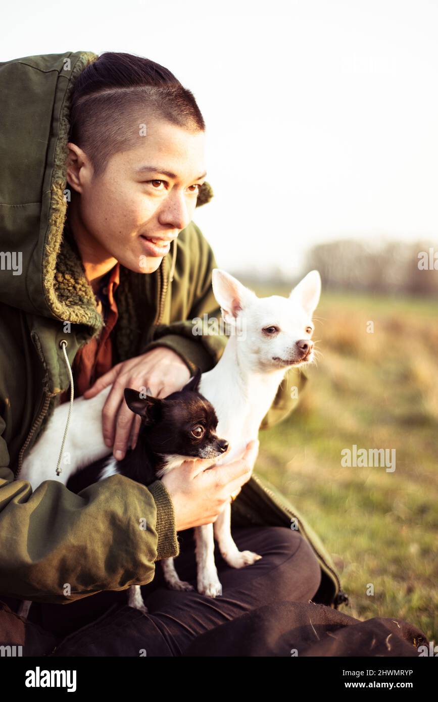 Geschlechtsbedingte Person blickt mit zwei niedlichen Hunden in die Nachmittagssonne Stockfoto