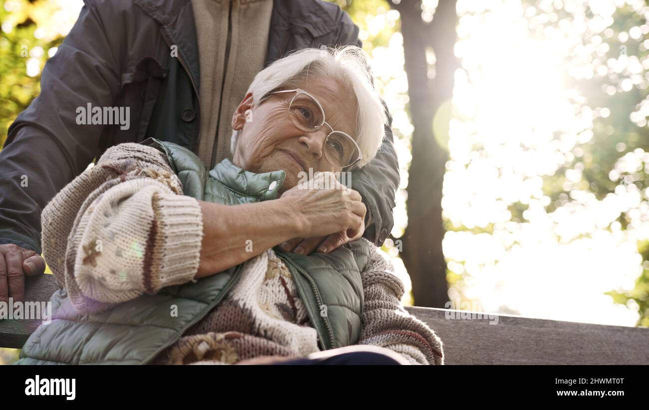 Die ruhige ältere Dame umarmt die Hand ihres pensionierten Mannes, während sie auf einer Bank in einem Park sitzt. Hochwertige Fotos Stockfoto