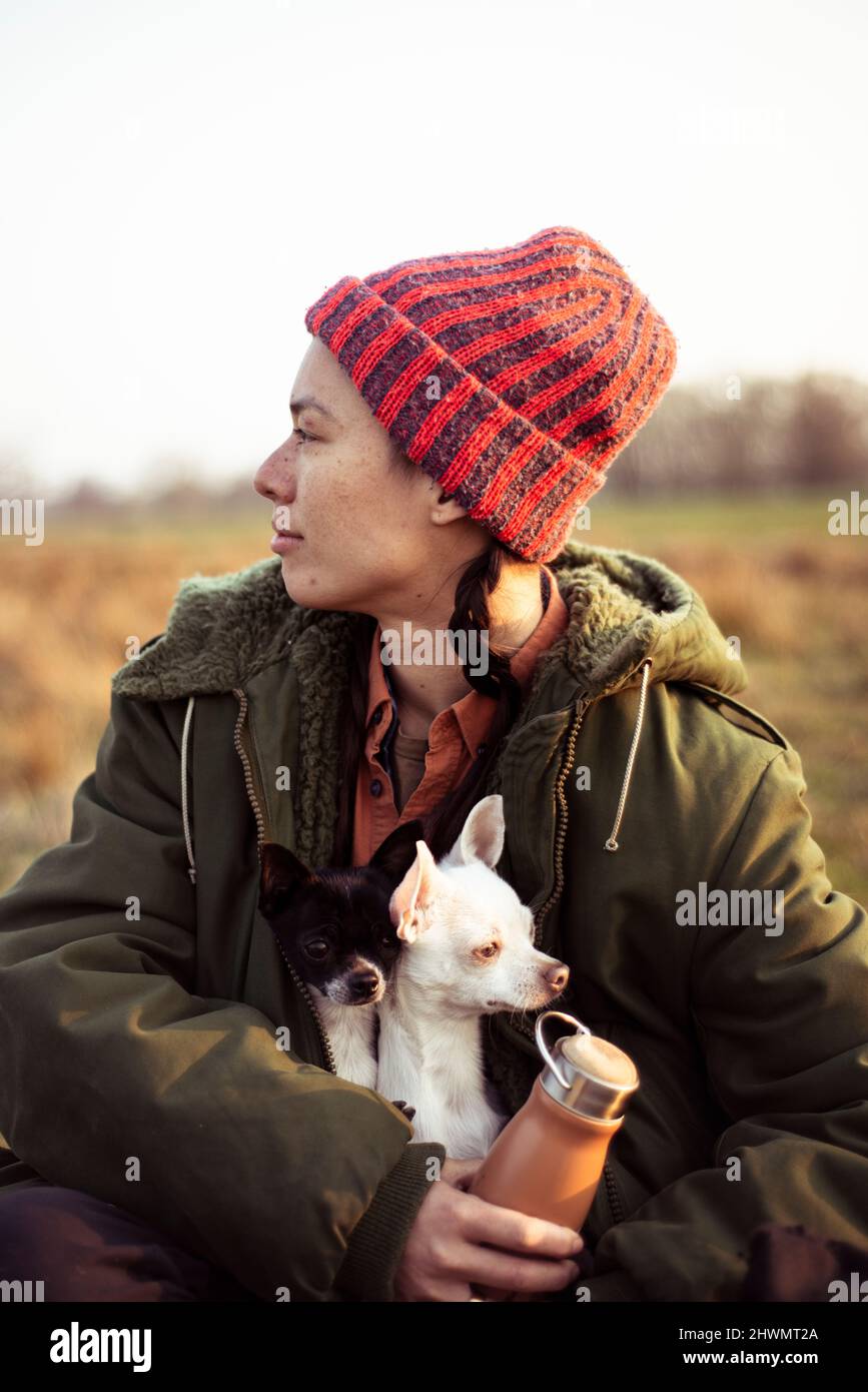 Gemischte ethnische Zugehörigkeit nicht-binäre Person sitzt im Feld in der Sonne mit zwei Hunden Stockfoto