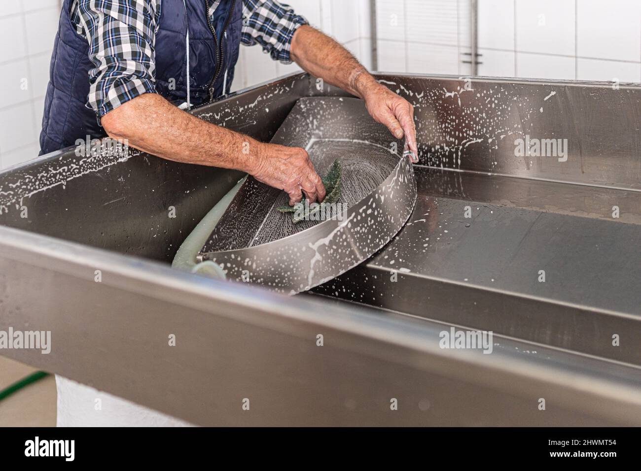 Nicht erkennbarer älterer Arbeiter, der ein Stück Metall mit einer Scheuermatte schrubbt Stockfoto