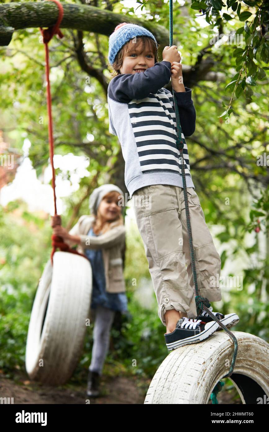 Schwingt das Leben. Aufnahme von zwei niedlichen Kindern, die in ihrem Garten auf Reifenschaukeln spielen. Stockfoto