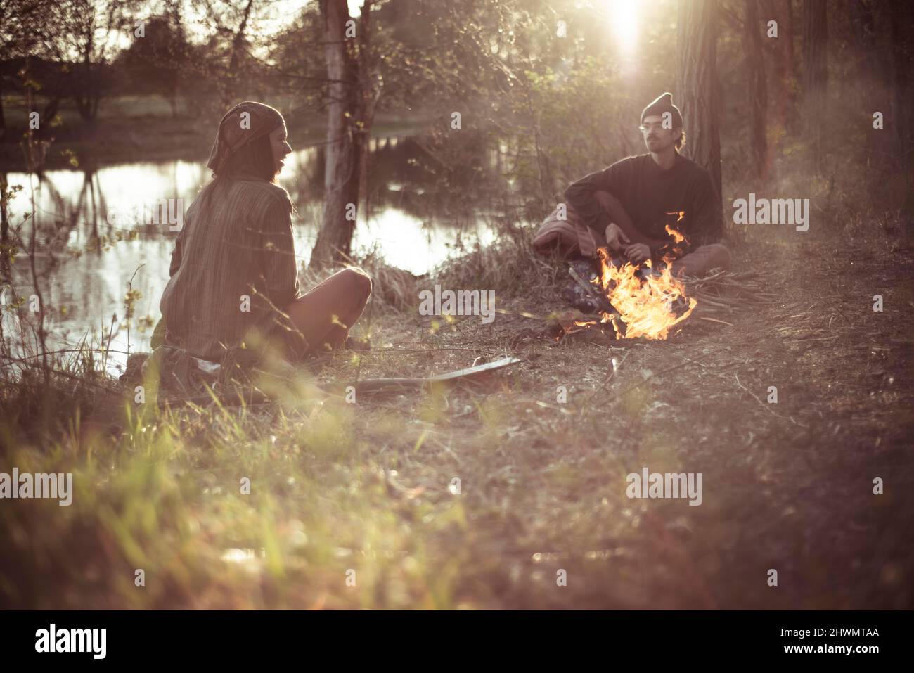 Freunde unterhalten sich im natürlichen Licht am Wasser um das Feuer Stockfoto