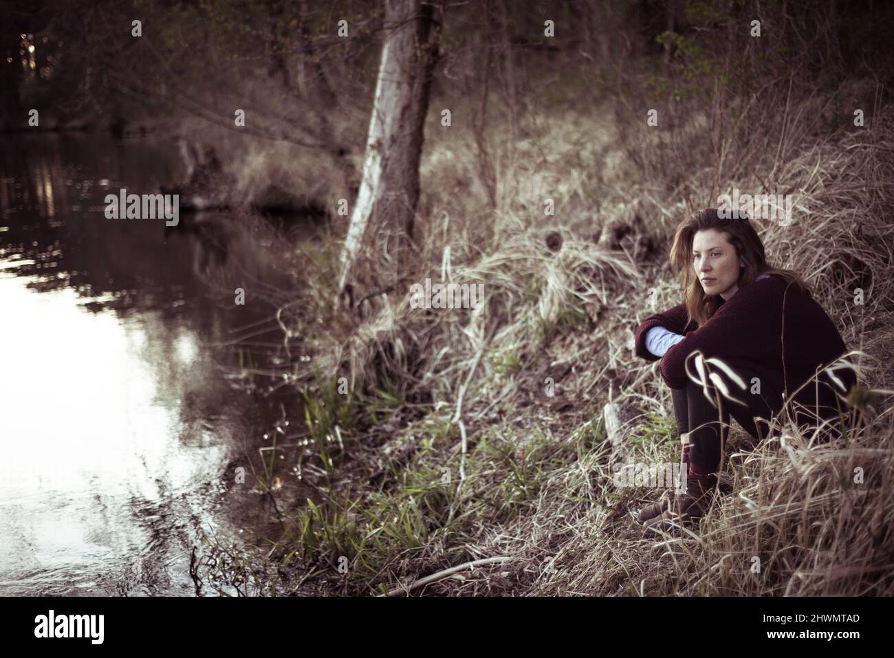 Schöne junge Frau betrachtet am Wasser sitzen in Schilf Stockfoto