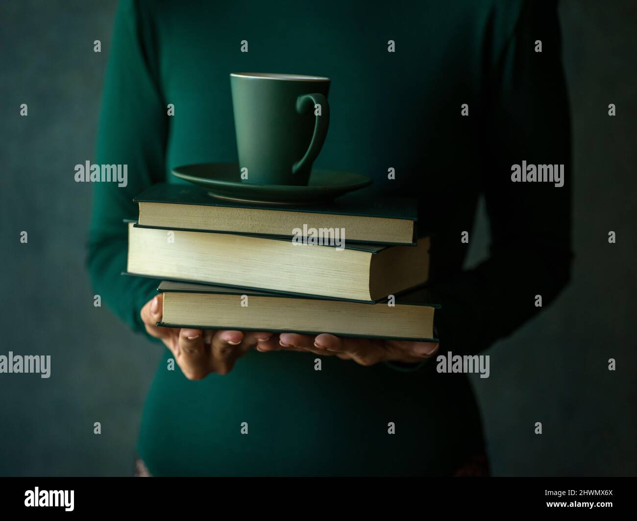 Mädchen in Grün hält ein paar Bücher und eine Tasse Kaffee Stockfoto