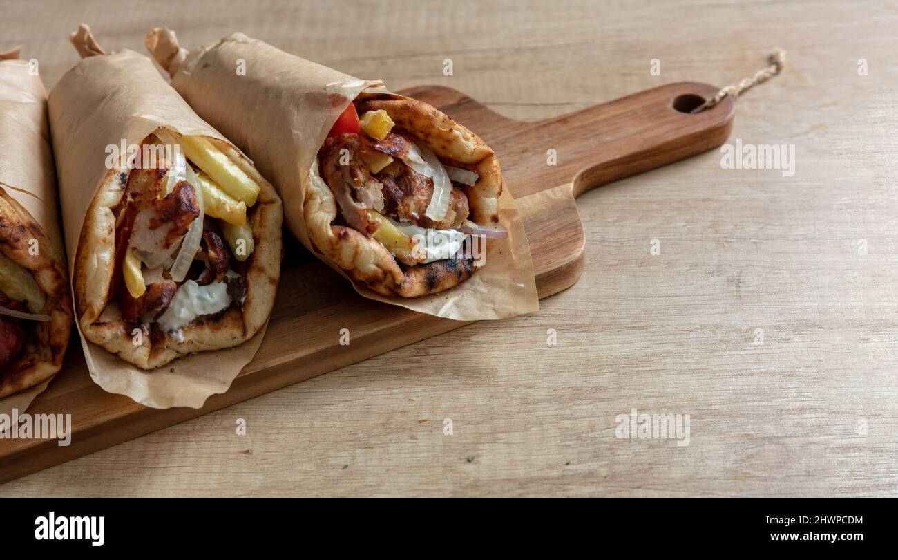 Shawarma Gyro Pita auf Holztisch. Griechische Lebensmittel, Fleisch in Scheiben, Kartoffeln, Tomaten und Zatziki, Papierverpackung, Nahaufnahme. Stockfoto