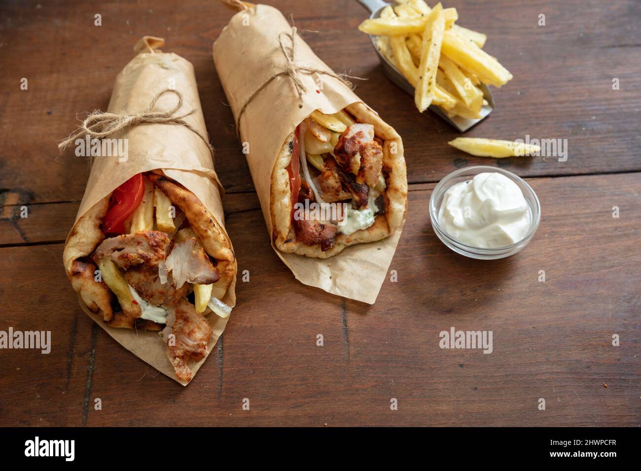 Shawarma Gyro Pita Brot auf Holztisch. Griechische Lebensmittel, Fleisch in Scheiben, Kartoffeln, Tomaten und Zatziki, Papierverpackung, Speicherplatz kopieren. Stockfoto