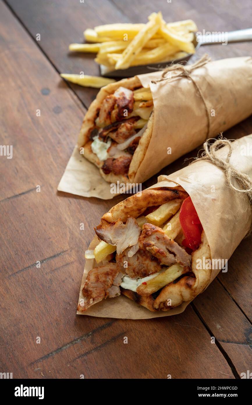 Gyro Shawarma Pita Brot auf Holztisch. Griechische Lebensmittel, Fleisch in Scheiben, Kartoffeln, Tomaten und Zatziki, Papierverpackung, Speicherplatz kopieren. Stockfoto