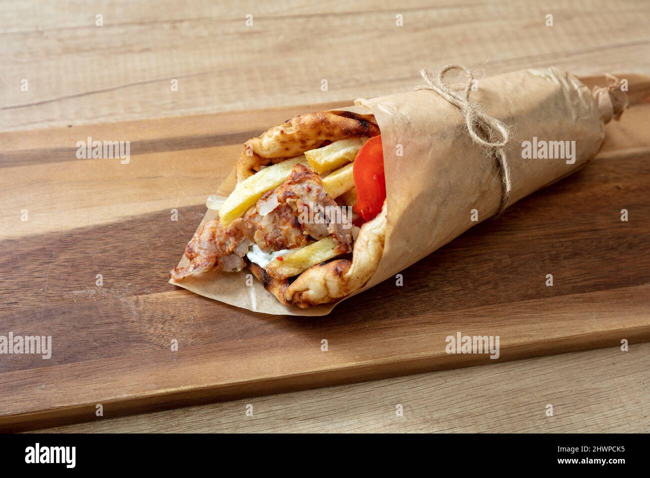 Gyro Pita Shawarma auf Holztisch. Griechische Lebensmittel, Fleisch in Scheiben, Kartoffeln, Tomaten und Zatziki, Papierverpackung, Nahaufnahme. Stockfoto