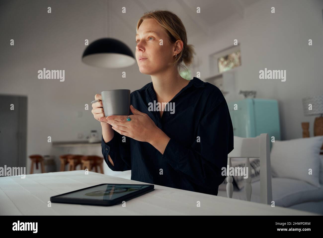 Kaukasische Modedesignerin trinkt Kaffee im Arbeitszimmer, während sie Mode auf einem digitalen Tablet entwirft Stockfoto