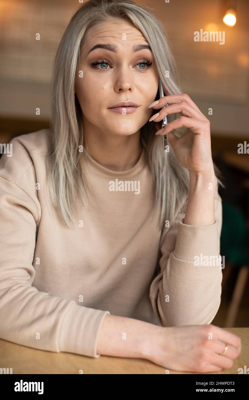 Vertikale Foto von überrascht verwirrt verrückt blonde Frau, starrte, sprechende Handy im Restaurant. Mein Freund ist spät, nahe Stockfoto