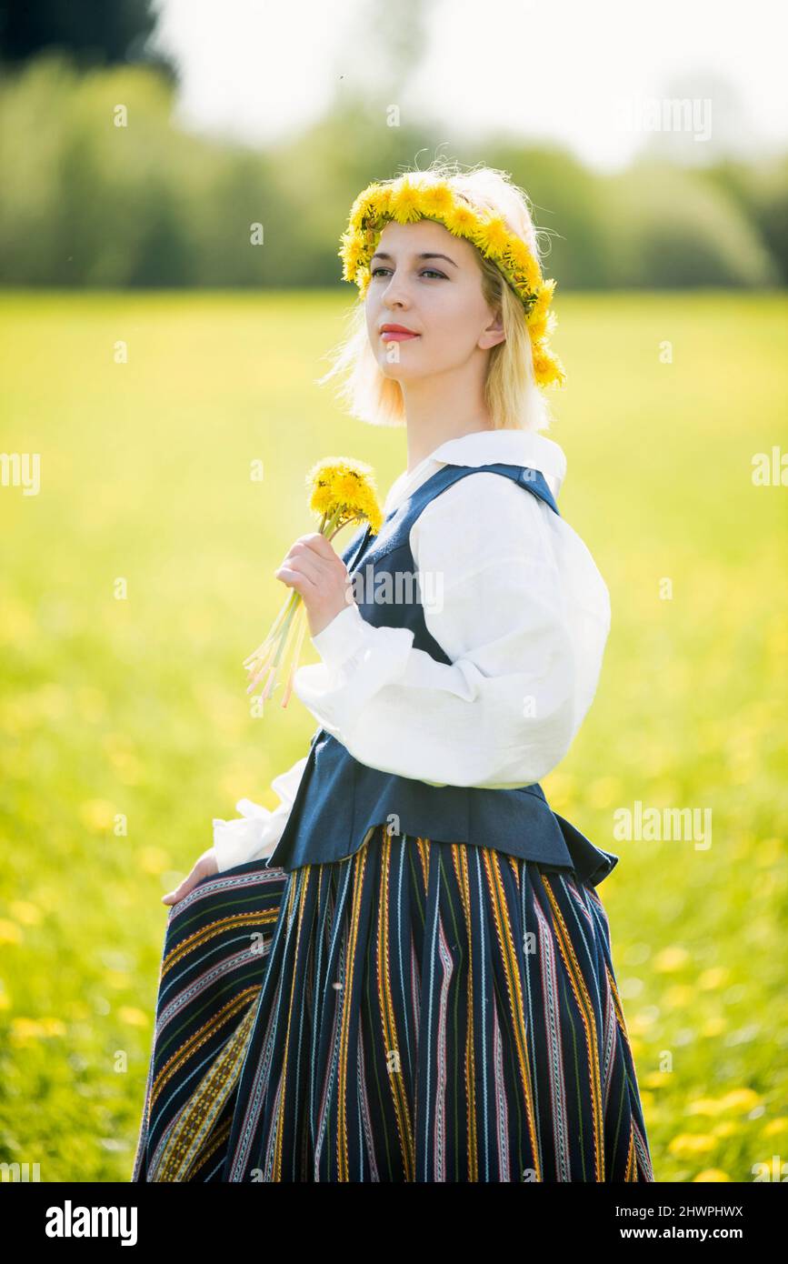 Junge Frau in Nationalkleidung mit gelbem Dandelion-Kranz im Frühlingsfeld. Frühling Stockfoto