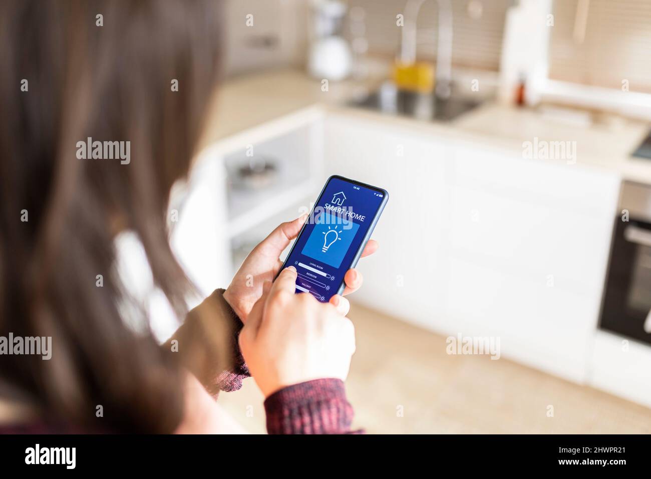 Frau, die die Helligkeit mithilfe der Smart-Home-Anwendung auf dem Mobiltelefon zu Hause anpasst Stockfoto