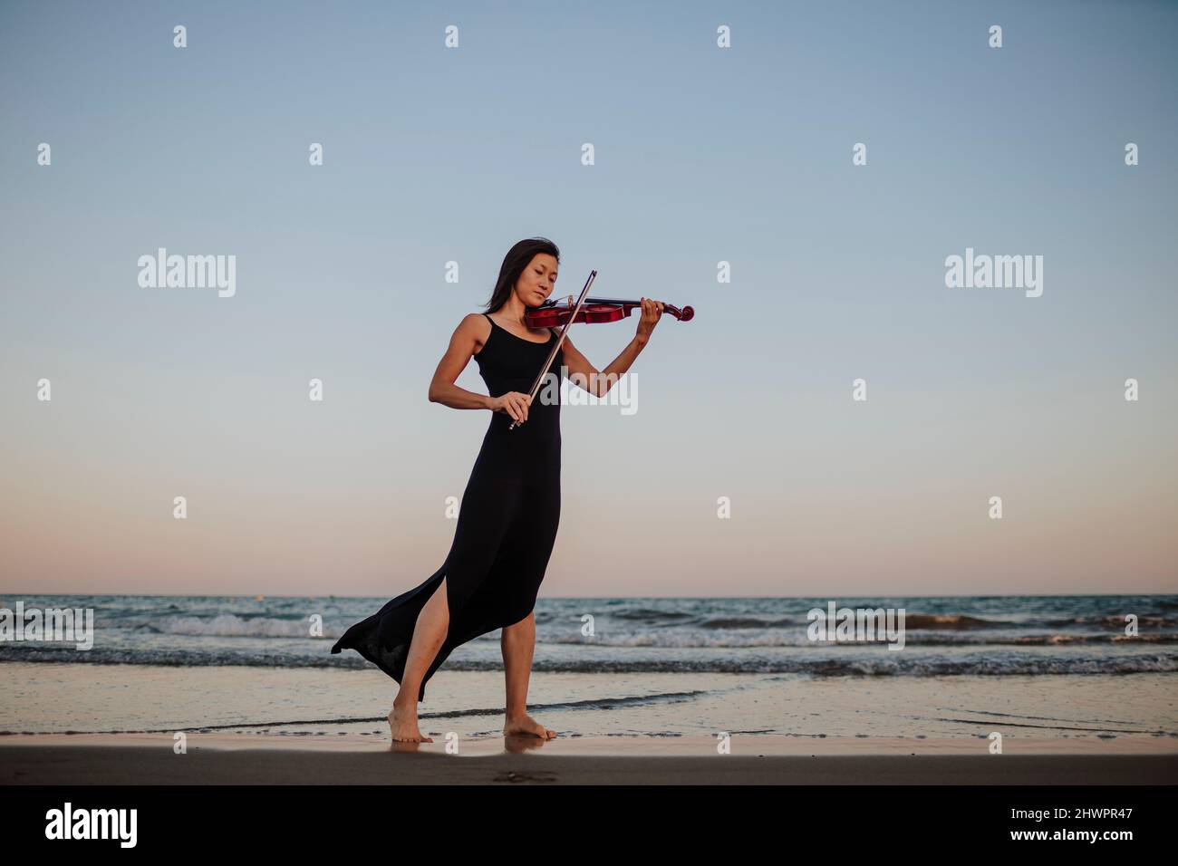 Frau, die am Strand Geige am Meer spielt Stockfoto
