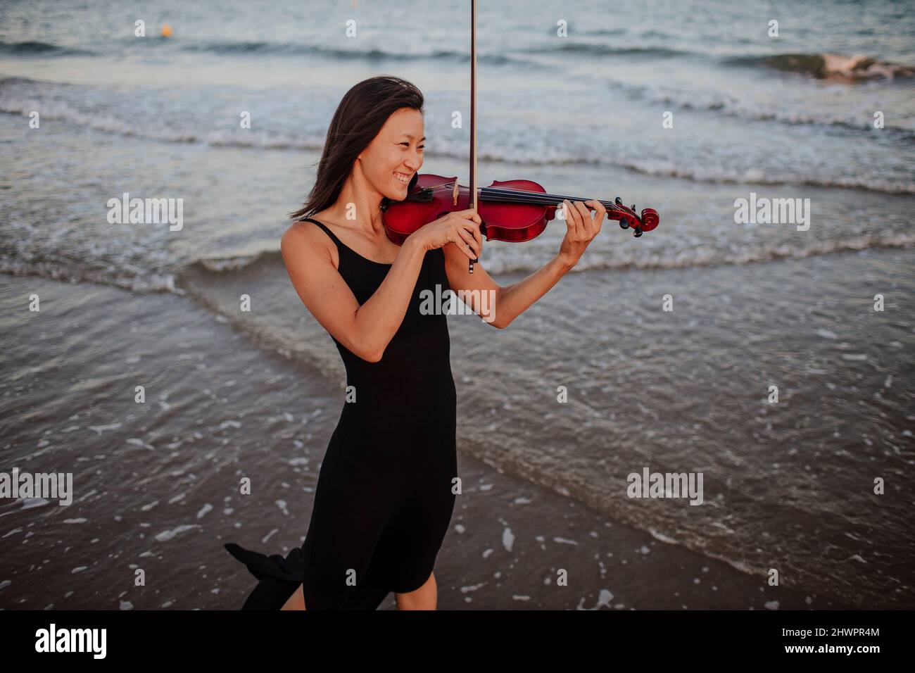 Glückliche Frau, die am Strand Geige im Meer spielt Stockfoto