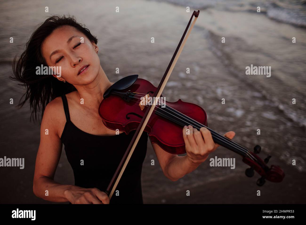 Frau spielt Geige im Meer am Strand Stockfoto