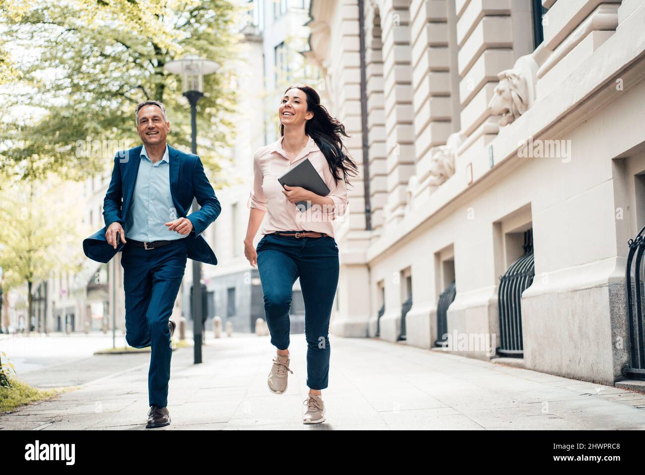 Fröhliche Geschäftsfrau und Geschäftsfrau, die auf dem Fußweg in der Stadt läuft Stockfoto