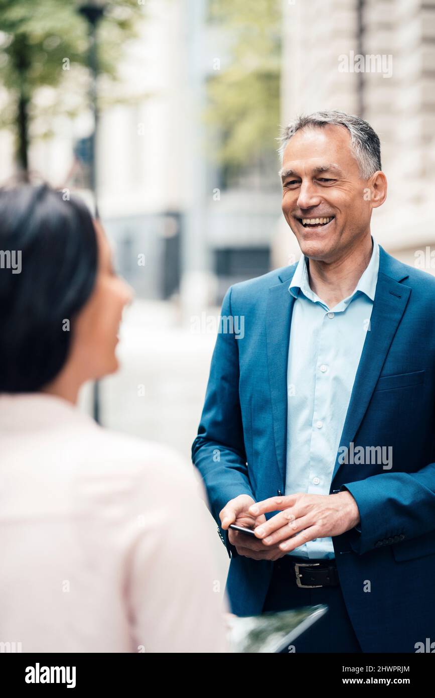 Fröhlicher reifer Geschäftsmann im Gespräch mit Geschäftsfrau auf dem Weg Stockfoto