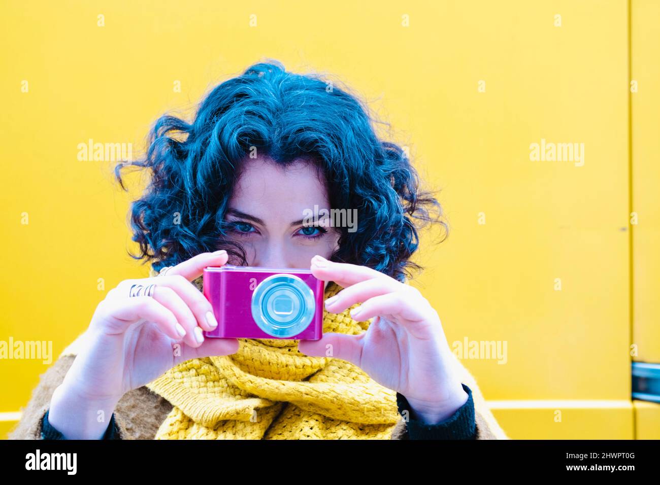 Frau fotografiert mit pinker Kamera vor der gelben Wand Stockfoto