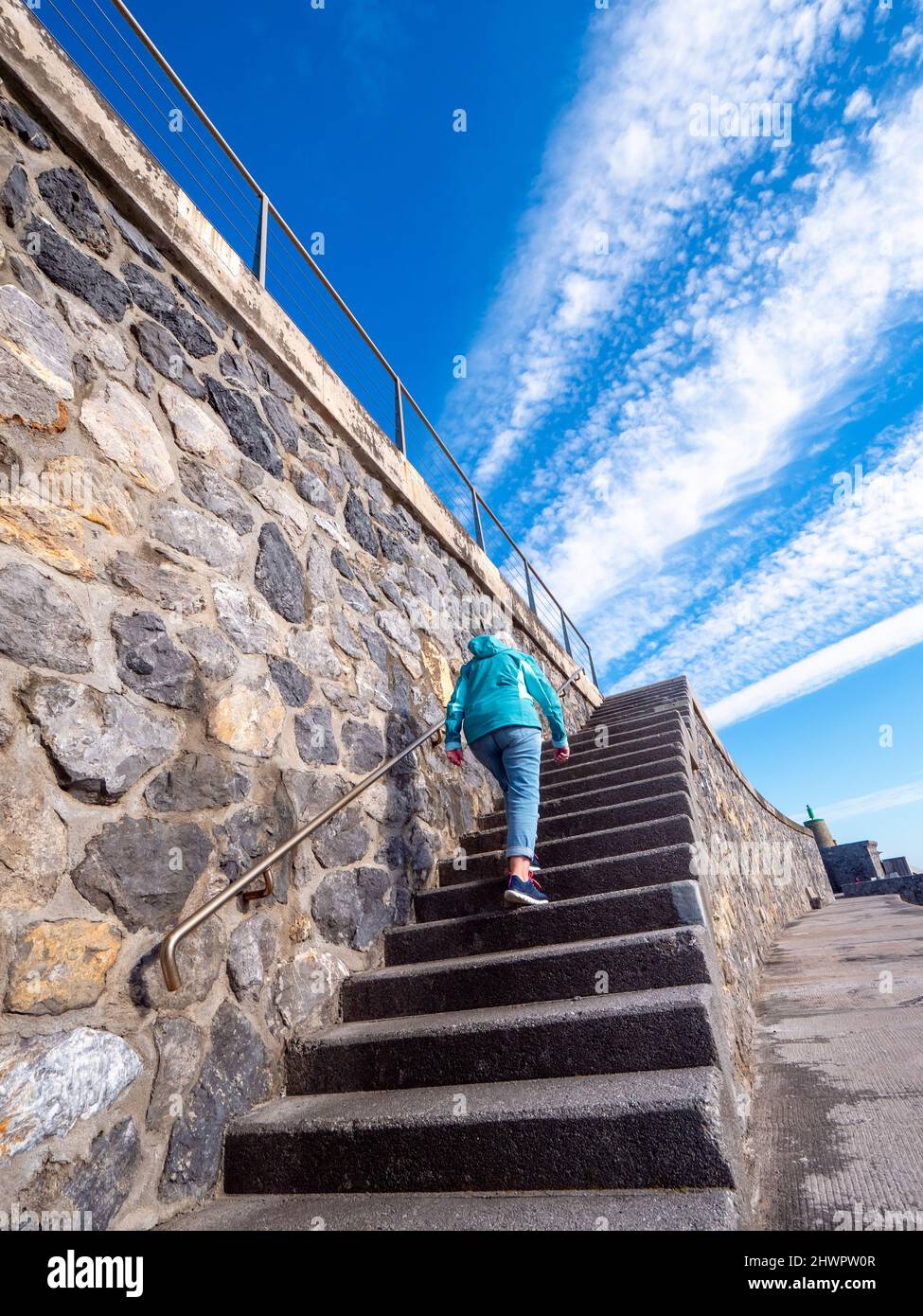 Ältere Frau, die sich auf Stufen an einer Steinmauer aufbewegt Stockfoto