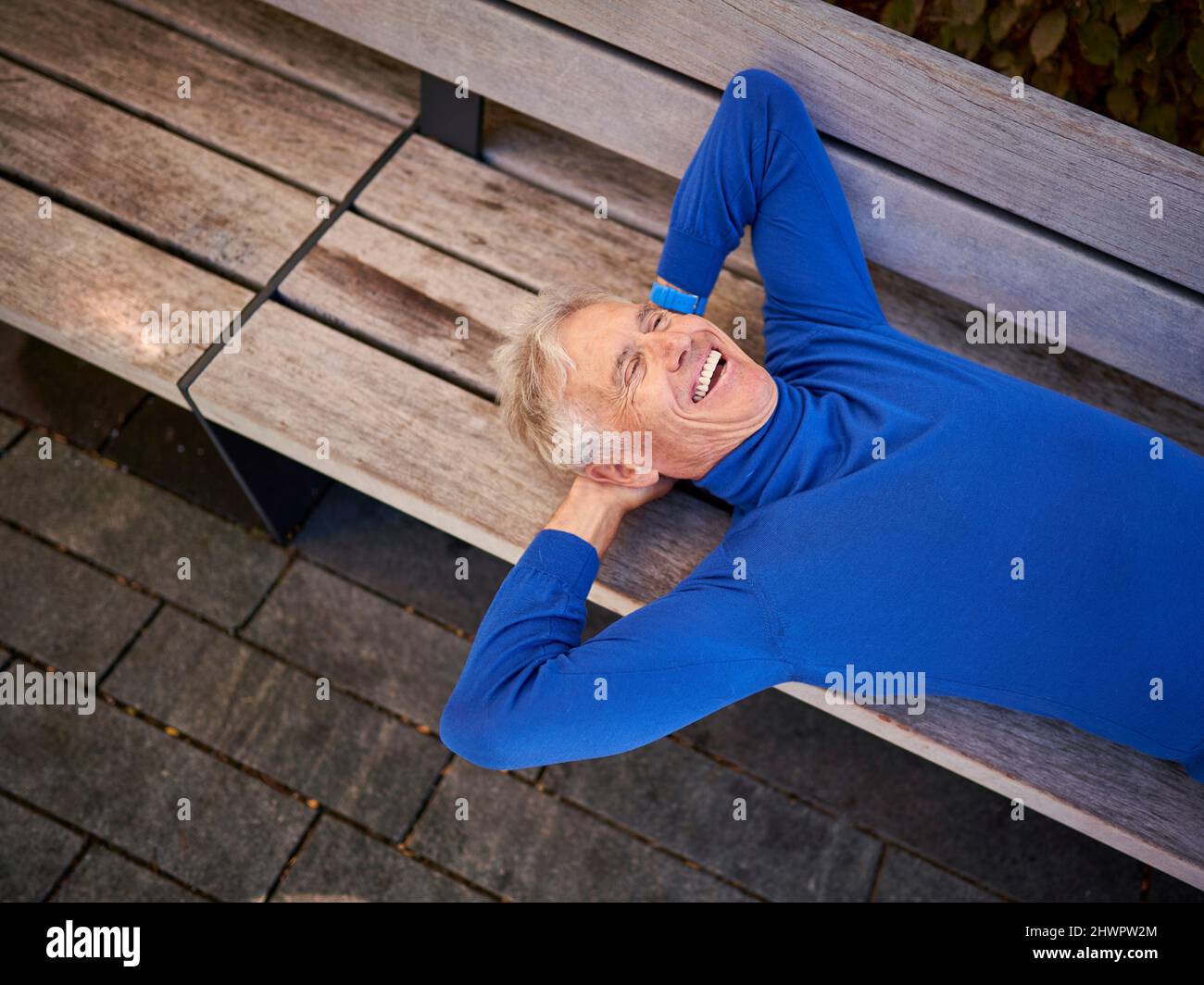 Älterer Mann, der lachend auf der Bank liegt Stockfoto