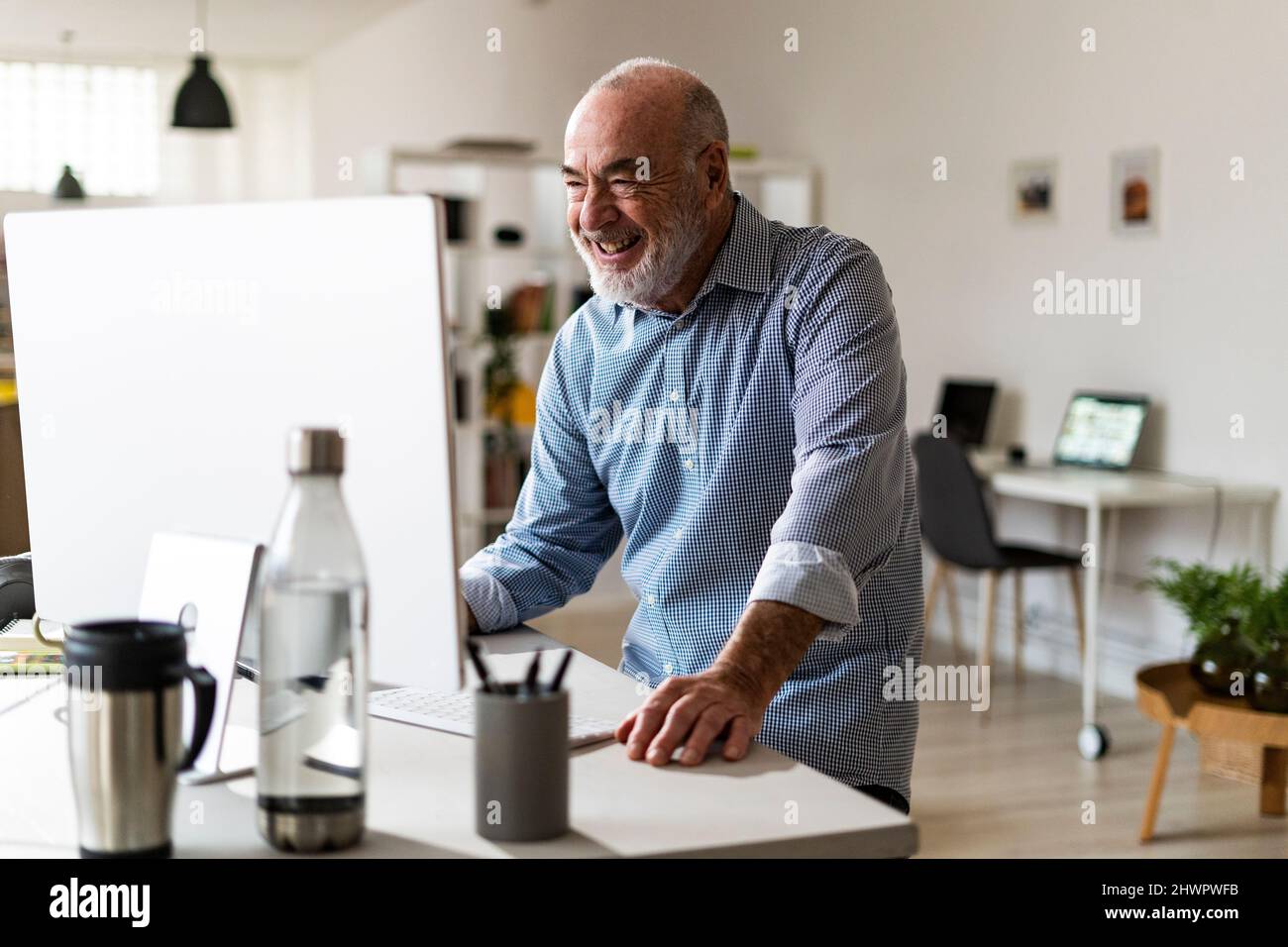 Fröhlicher Geschäftsmann, der am Schreibtisch einen Computer benutzt Stockfoto