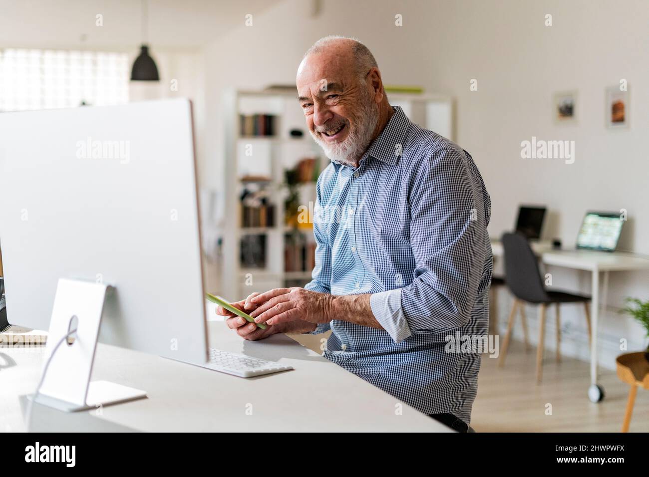 Fröhlicher Geschäftsmann mit Mobiltelefon am Schreibtisch Stockfoto