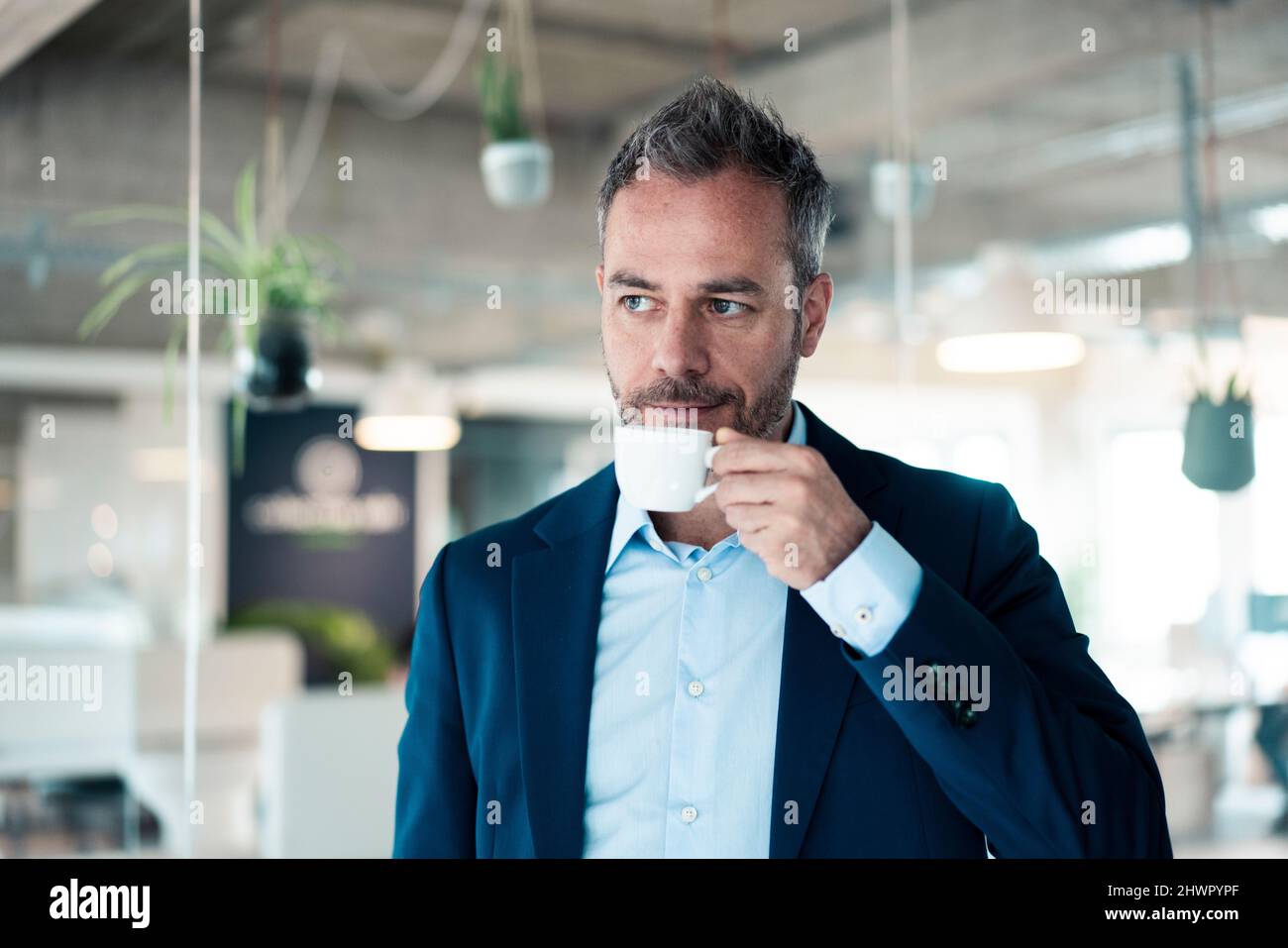 Nachdenklicher Geschäftsmann, der am Arbeitsplatz Kaffee trinkt Stockfoto