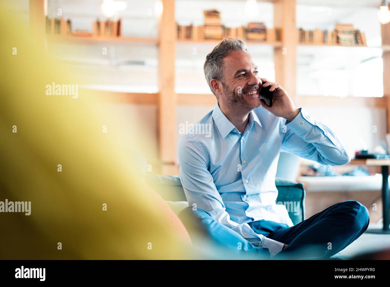 Fröhlicher Geschäftsmann, der am Arbeitsplatz mit dem Mobiltelefon spricht Stockfoto