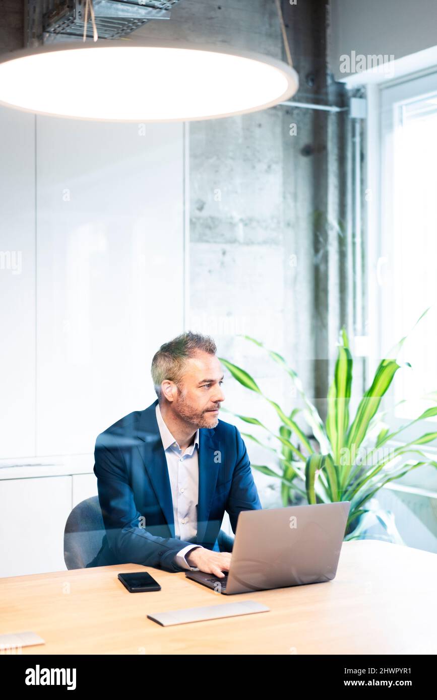 Selbstbewusster Geschäftsmann, der am Arbeitsplatz mit einem Laptop sitzt Stockfoto