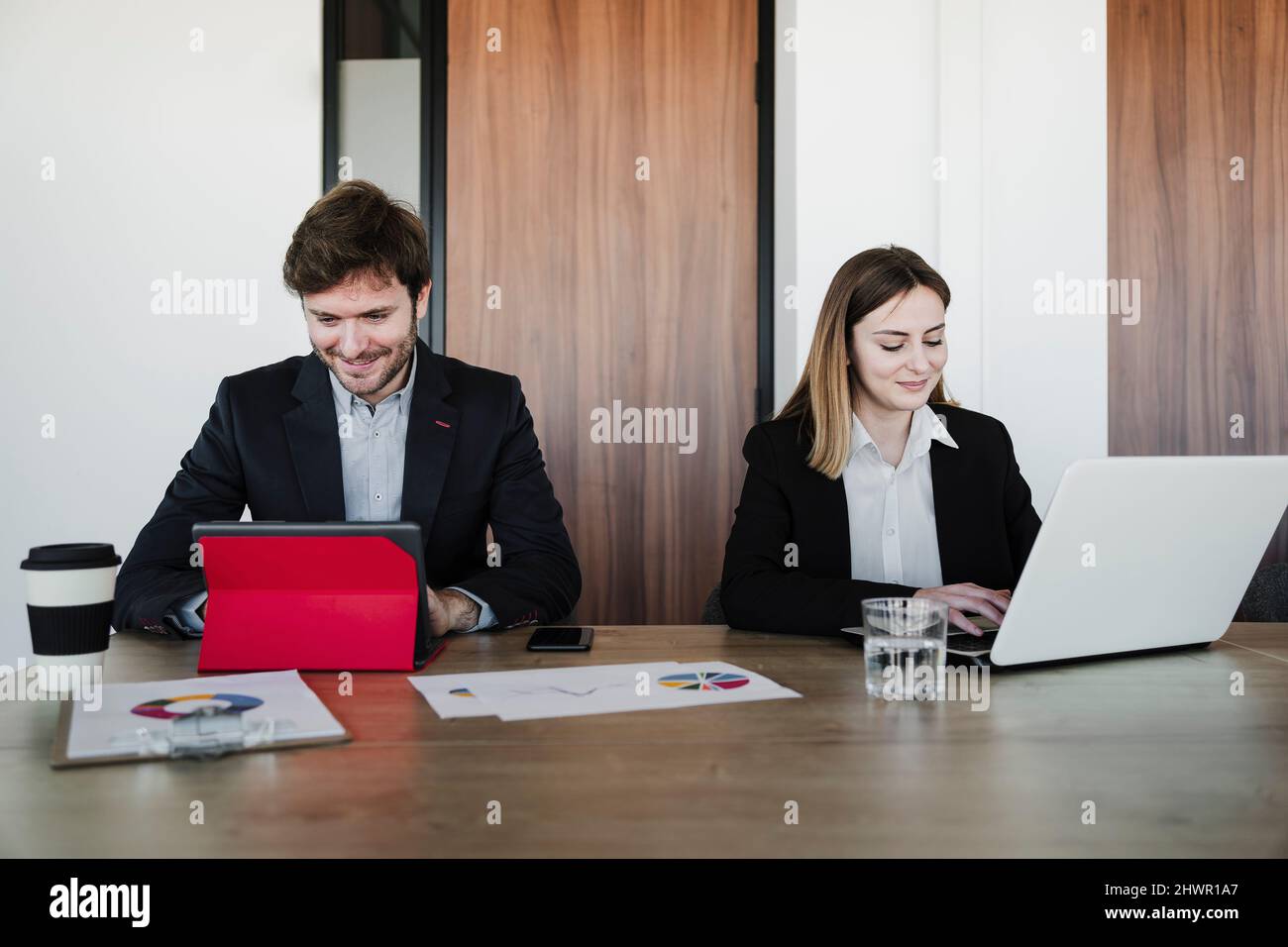 Lächelnde Kollegen aus der Wirtschaft nutzen drahtlose Technologien am Schreibtisch im Coworking-Büro Stockfoto