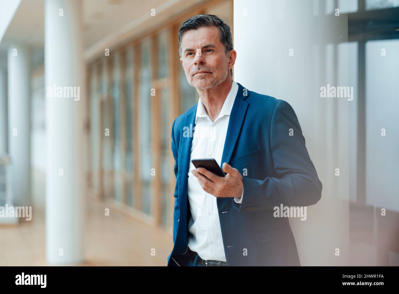 Geschäftsmann mit Smartphone in der Nähe der Säule im Büro Stockfoto