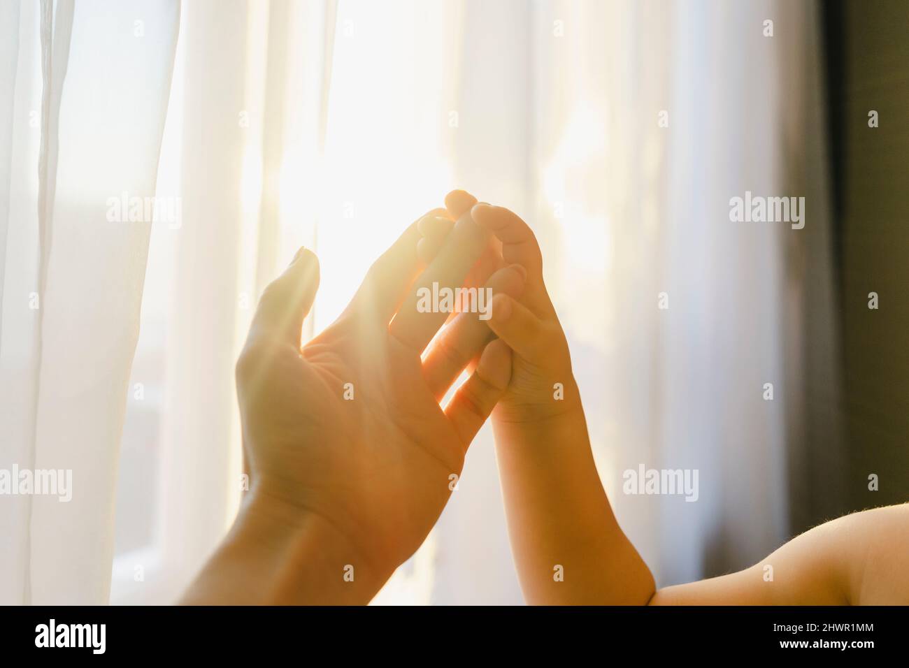 Junge, der zu Hause die Hand der Mutter vor dem Vorhang berührt Stockfoto