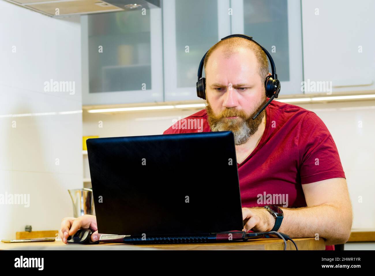 Erwachsene Person im Headset, die von zu Hause aus mit einem Laptop arbeitet. Reifer Mann konzentriert sich während Online-Meetings, Remote-Job-Konzept Stockfoto